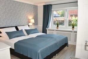 A bedroom with a bed, a window with curtains, a radiator, and a wall with a textured pattern. - at the sailing school (Heiligenhafen)
