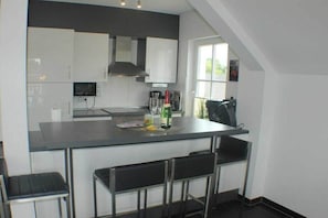 A modern kitchen with white cabinets, a central island with bar stools, and a window providing natural light. - Holiday apartment with 2 bedrooms (Wendisch Rietz)