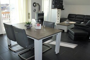 A modern living room with a dining table, chairs, a sofa, and a television.