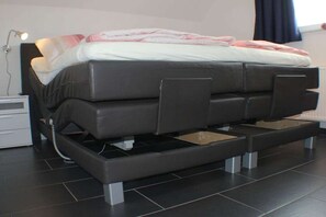 A modern bed with storage drawers underneath, a bedside table with a lamp, and a window with curtains.