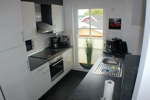 A compact kitchen with white cabinets, a black countertop, a built-in oven, a coffee maker, and a window with a view of a house.