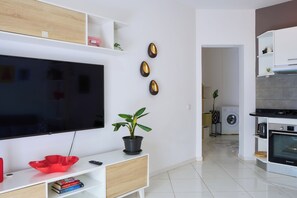A modern living room with a flat-screen TV, a red decorative bowl, a potted plant, and a kitchen area with a washing machine and oven. - Bright Apartment in Santa Maria (Sal)