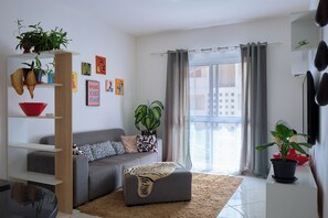 A modern living room with a grey sofa, a red bowl on a shelf, and various plants. - Bright Apartment in Santa Maria (Sal)