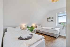 Een slaapkamer met twee bedden, een groot raam en een plant.