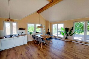 Een ruime keuken met een eethoek, grote ramen en houten vloeren.