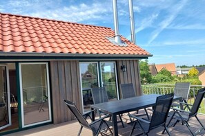 Een modern terras buiten, met een dak van rode tegels, een glazen ingang en een eethoek met stoelen en een tafel.