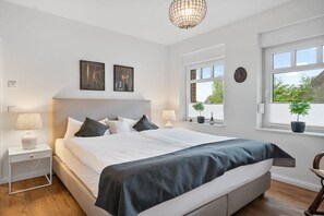Een slaapkamer met een bed, nachtkastjes, een kroonluchter en ramen met planten.