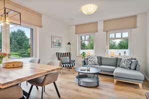 Een ruime woonkamer met een houten eettafel, een grijze bank en een gestreepte fauteuil.