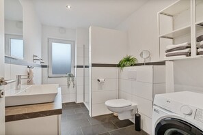 Een moderne badkamer met een groot wastafel, toilet en een wasmachine.