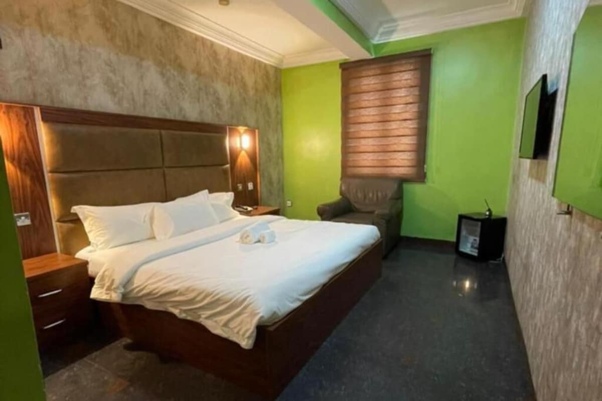 Een hotelkamer met een bed, een nachtkastje, een stoel, een televisie en een wandlamp.