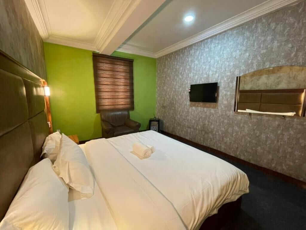 Ein Hotelzimmer mit einem Bett, einem an der Wand befestigten Fernseher und einem Fenster mit Jalousien.