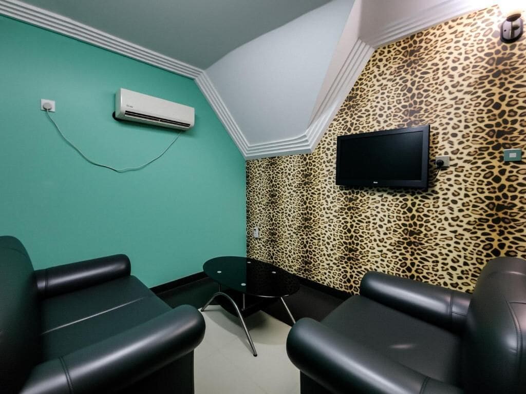 Una habitación con paredes color turquesa, un televisor montado y un papel tapiz de estampado de leopardo. Hay dos sillas negras y una mesita.