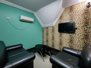 A room with teal walls, a mounted TV, and a leopard print wall. There are two black chairs and a small table. - Aotel Hotel Lagos Ago (Lagos)