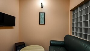 Un saló amb un sofà de cuir negre, una taula rodona de fusta, una obra d'art abstracta emmarcada a la paret i un televisor muntat sobre el sofà.