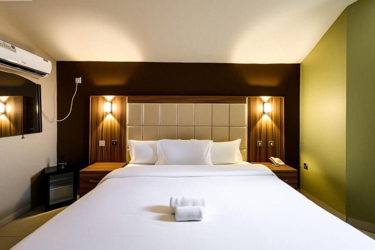 Een hotelkamer met een groot bed, twee nachtkastjes, een wandairconditioner en twee wandlampen.