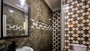 Un bany amb un lavabo blanc, un mirall, una vàter i rajoles amb dibuixos a les parets.