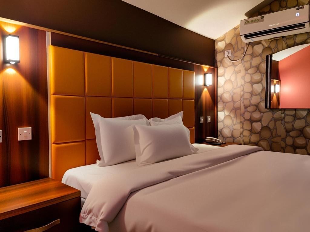 Habitación de hotel con una cama grande, cabecera de madera, pared con diseño de piedra y aire acondicionado instalado.