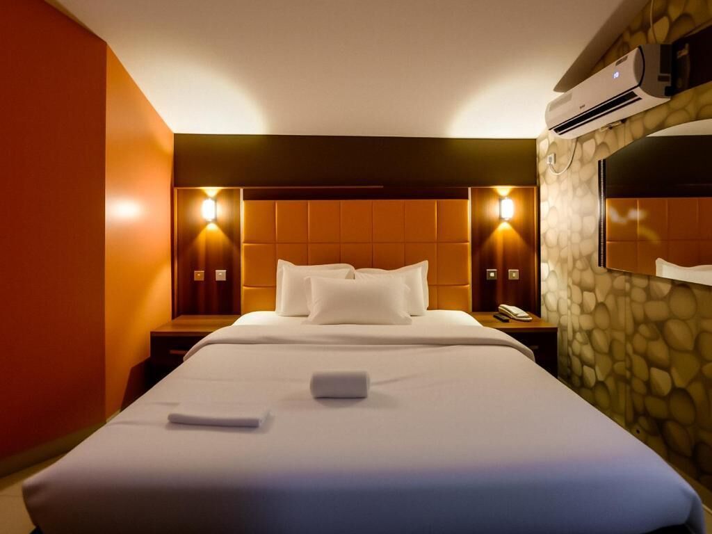 Habitación de hotel con una cama grande, dos mesitas de noche, aire acondicionado de pared y una pared de acento de piedra.