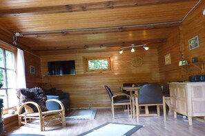 A wooden cabin interior with a dining area, a sofa, and a television. - Holiday home Berghaus (Reinhardshagen)