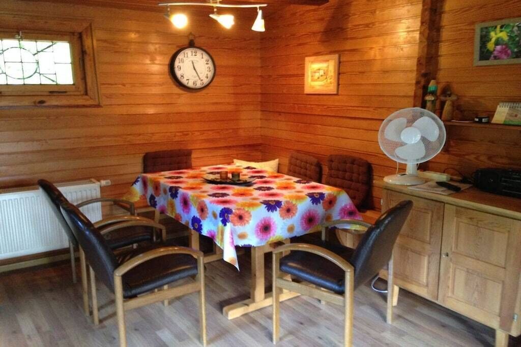 Ein Interieur einer Holzhütte mit einem Esstisch, Stühlen, einer Uhr, einem Ventilator und einem Fenster mit Blick.