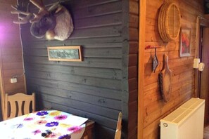 Een kamer met een tafel bedekt met een bloemistisch tafelkleed, een gebeeldhouwd dierenhoofd aan de muur en een ingelijste foto.