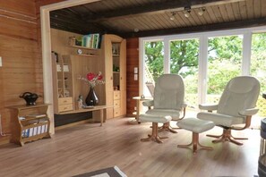 A wooden interior with a bookshelf, two armchairs, and a large window. - Holiday home Berghaus (Reinhardshagen)