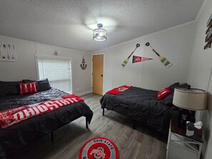 A room with two beds, a ceiling fan, a lamp, and a door. - Buckeye Island Paradise (Put-in-Bay Township)