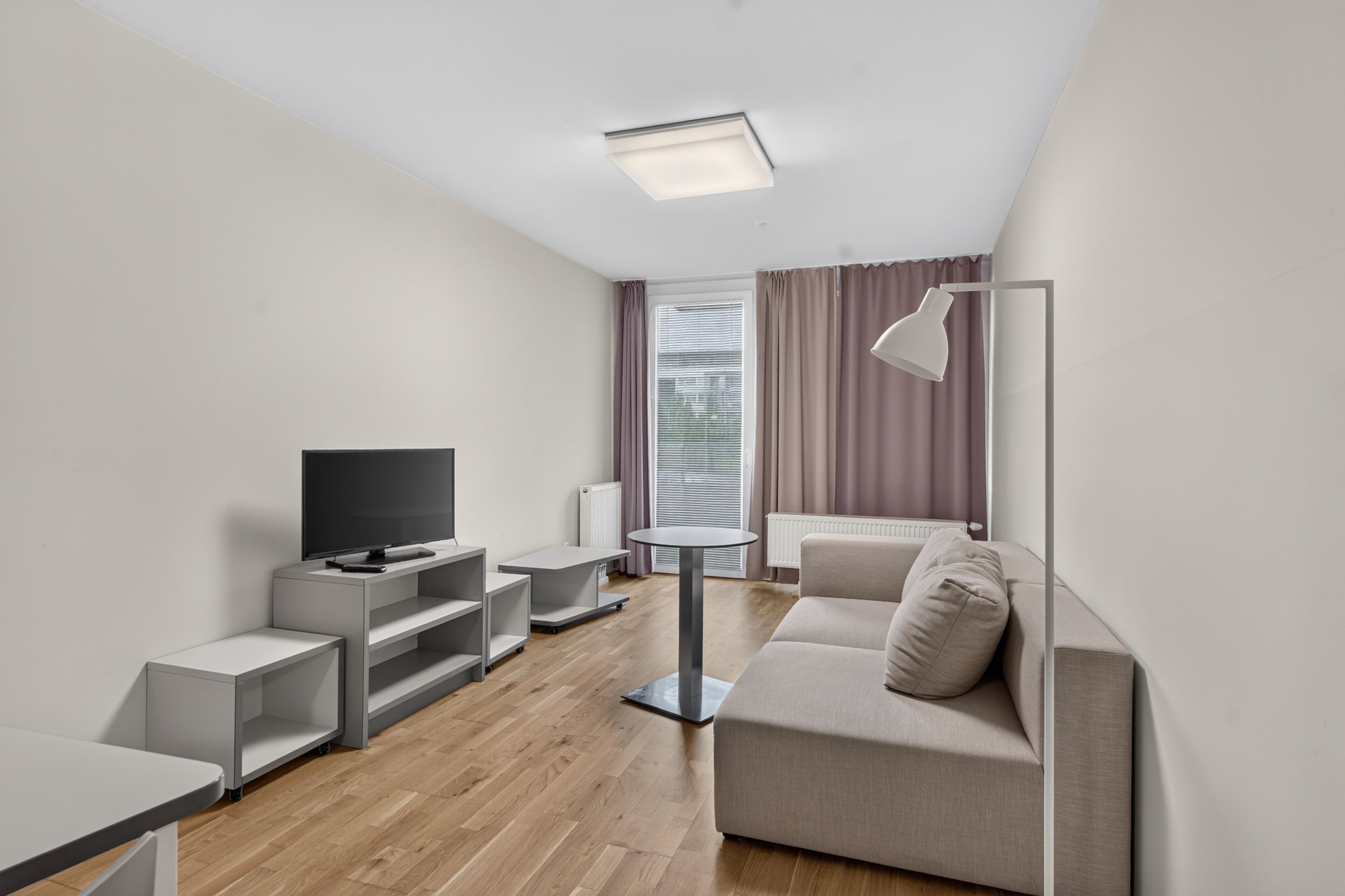 Una sala de estar moderna con un televisor de pantalla plana, un sofá gris, una mesita y una lámpara de pie.