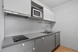 Una cocina moderna con microondas integrado, pileta de acero inoxidable y muebles grises.