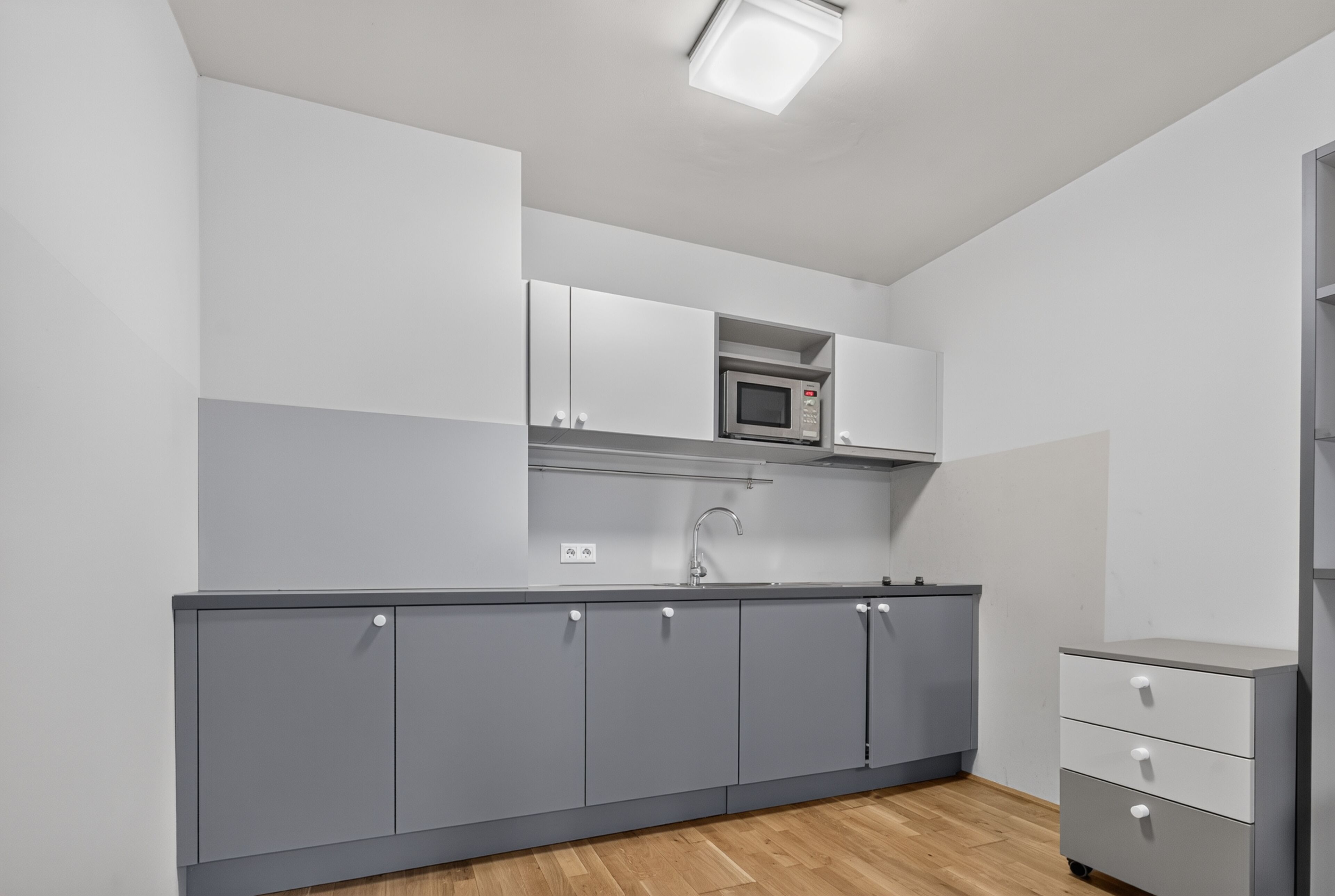 A modern kitchen with grey cabinets, a microwave, and a sink.