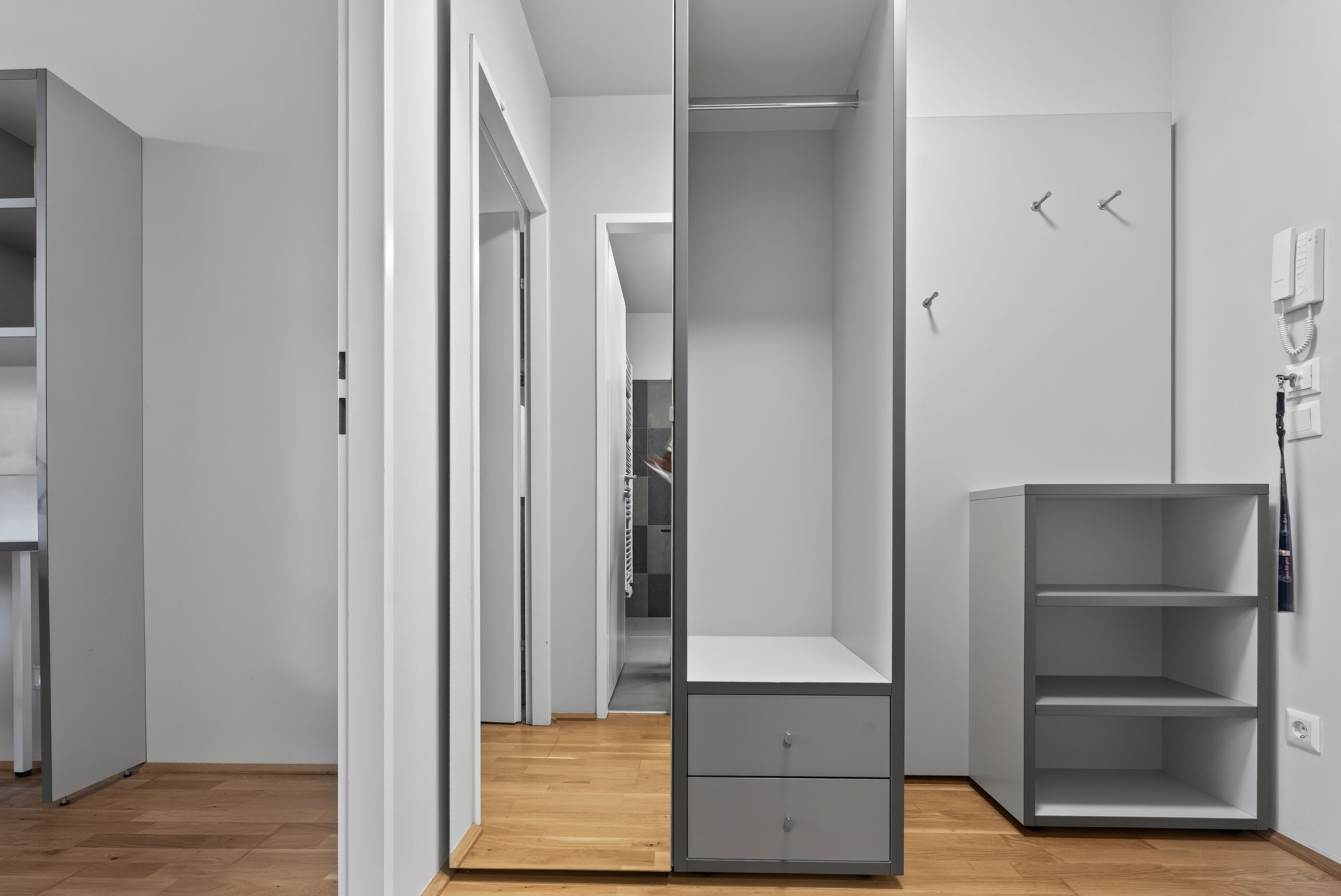 A modern, minimalist room with a built-in wardrobe, a small desk, and a shelving unit.