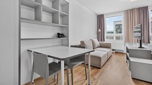 A modern, minimalist room with a dining table, two chairs, a sofa, and a small kitchenette area.