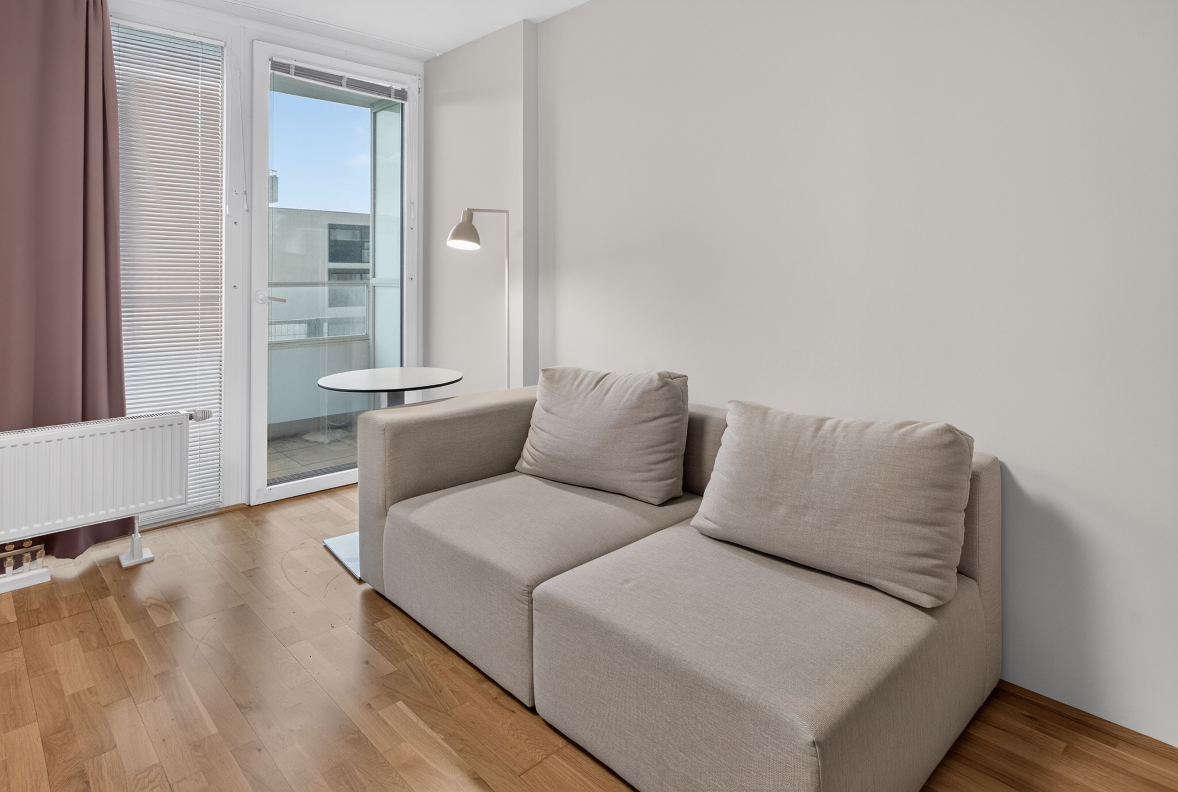 A modern living room with a beige sofa, a small round table, and a floor lamp.