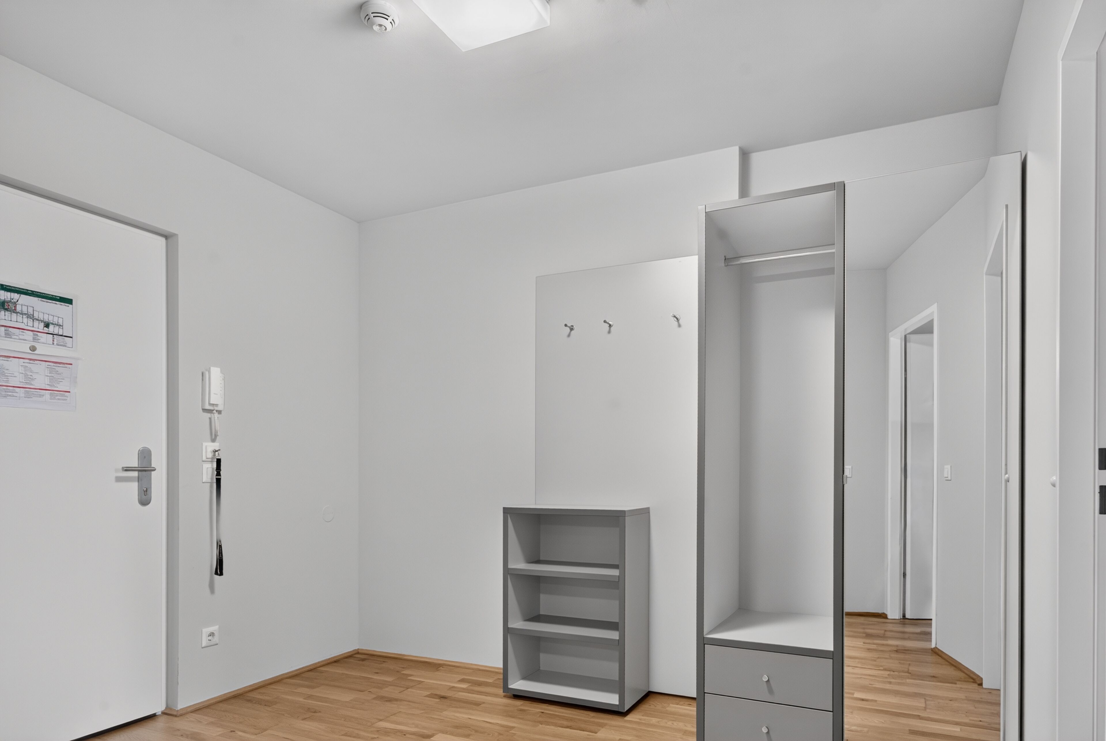 A modern, minimalistic room with a wooden floor, white walls, and a built-in wardrobe with multiple shelves and drawers.