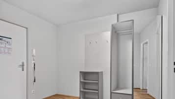 Une chambre moderne et minimaliste, dotée d’un plancher en bois, de murs blancs et d’une armoire intégrée avec de nombreuses étagères et tiroirs.