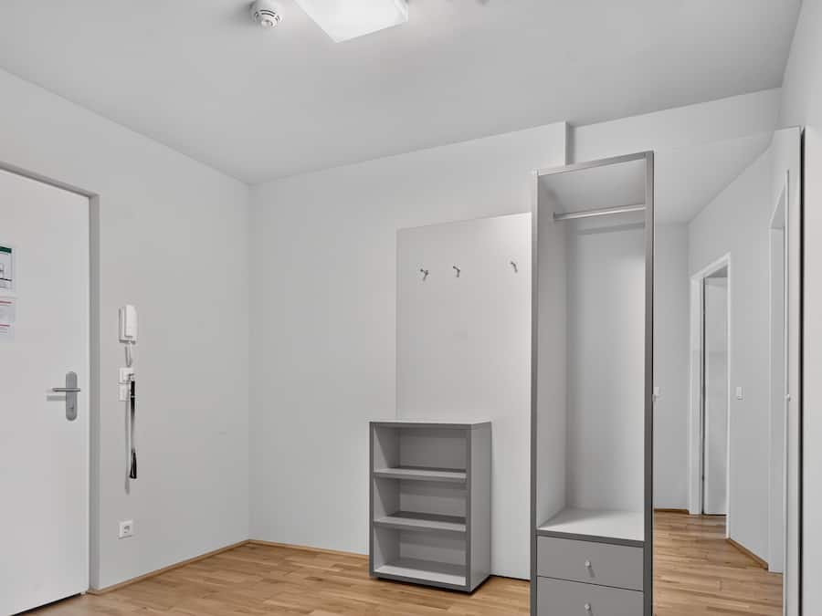 Una habitación moderna y minimalista con suelo de madera, paredes blancas y un armario empotrado con múltiples estantes y cajones.