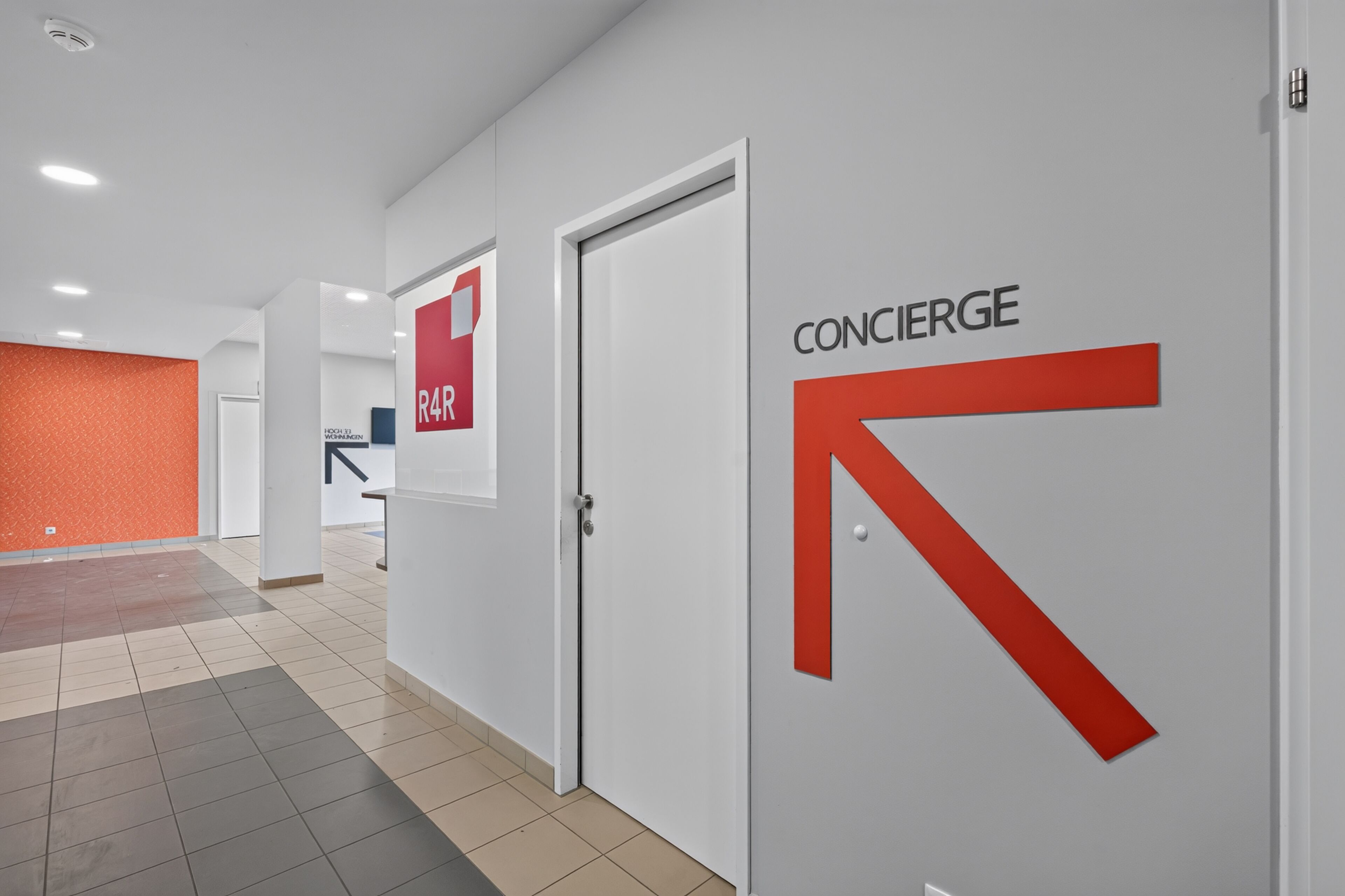 Ein Korridor mit einer weißen Tür, auf der 'CONCIERGE' steht, und einem roten Pfeil.