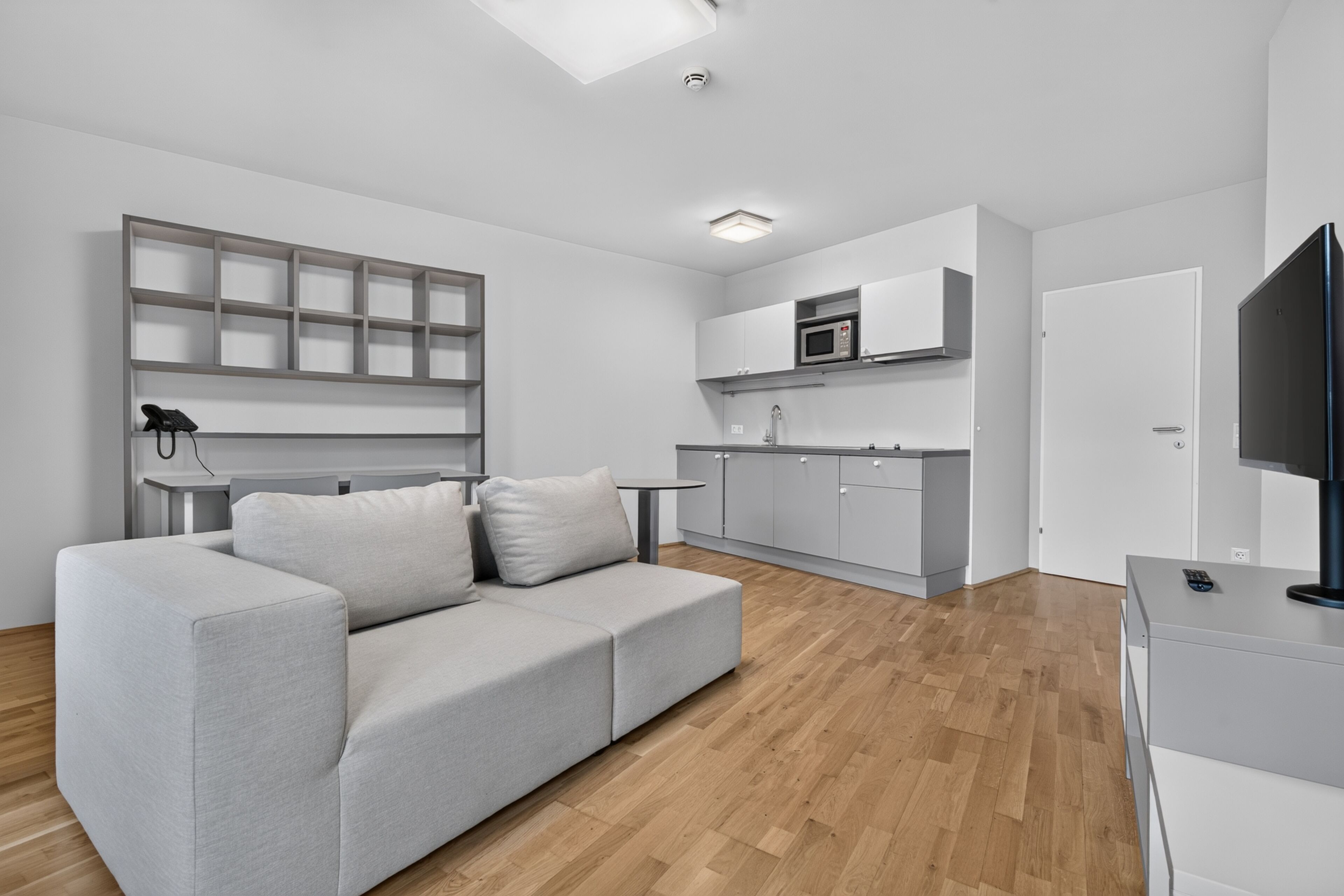 A modern living room with a grey sofa, a flat-screen TV, and a wooden floor.
