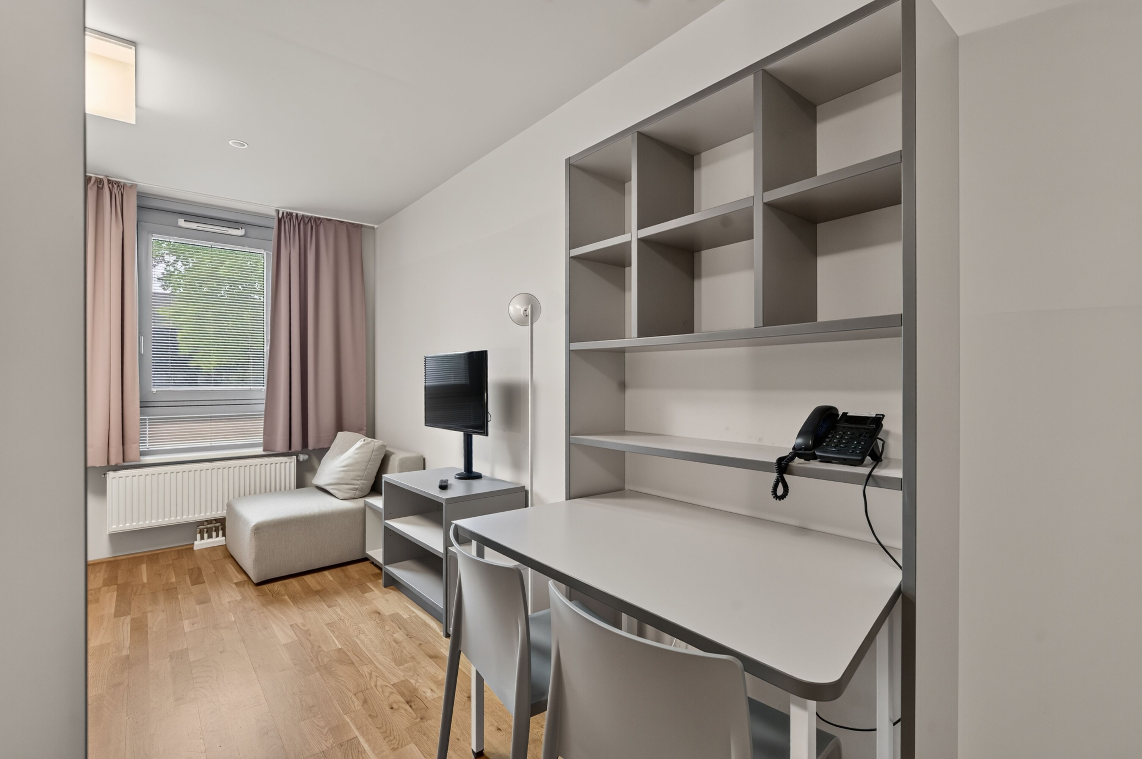Ein modernes Zimmer mit einem weißen Schreibtisch, einem Stuhl, einem Fernseher und einem Telefon.