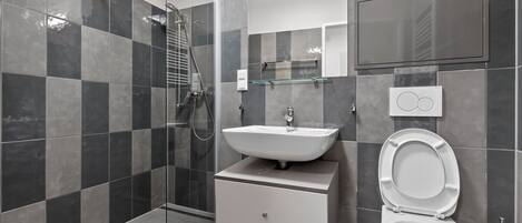 Un baño moderno con cabina de ducha de vidrio, un lavabo blanco y un inodoro.