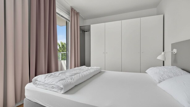 A modern bedroom with a large bed, a wardrobe, and a window with curtains.