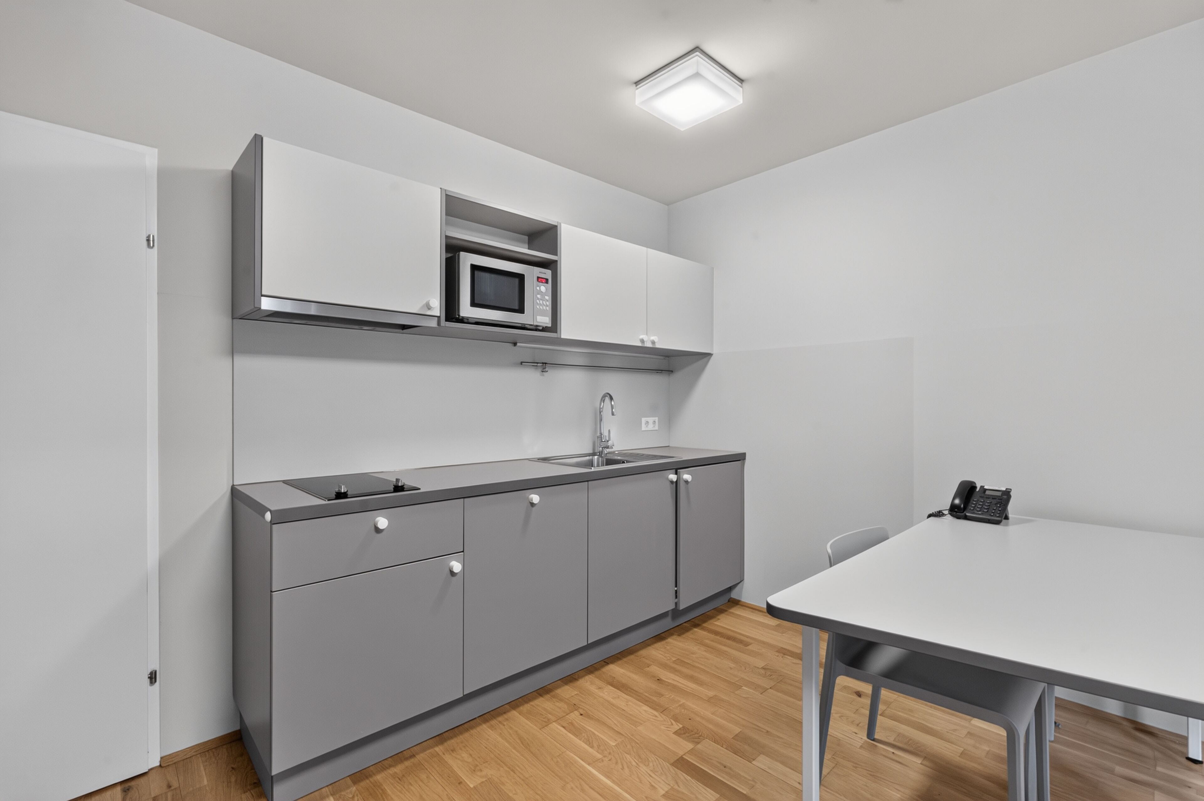 A compact kitchen with a microwave, sink, and a table with a phone.