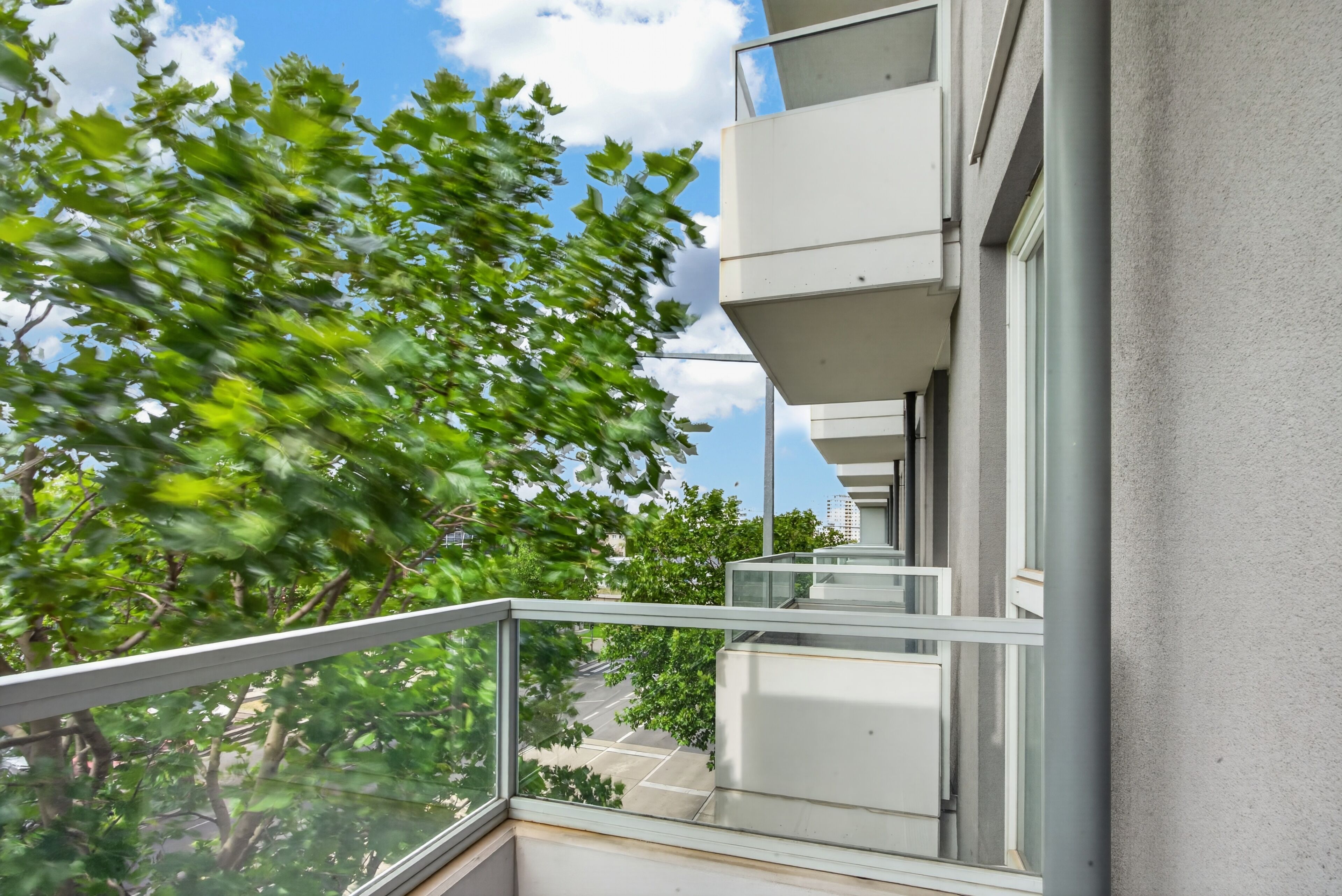 Een modern gebouw met een glazen balkon dat uitkijkt over een straat.