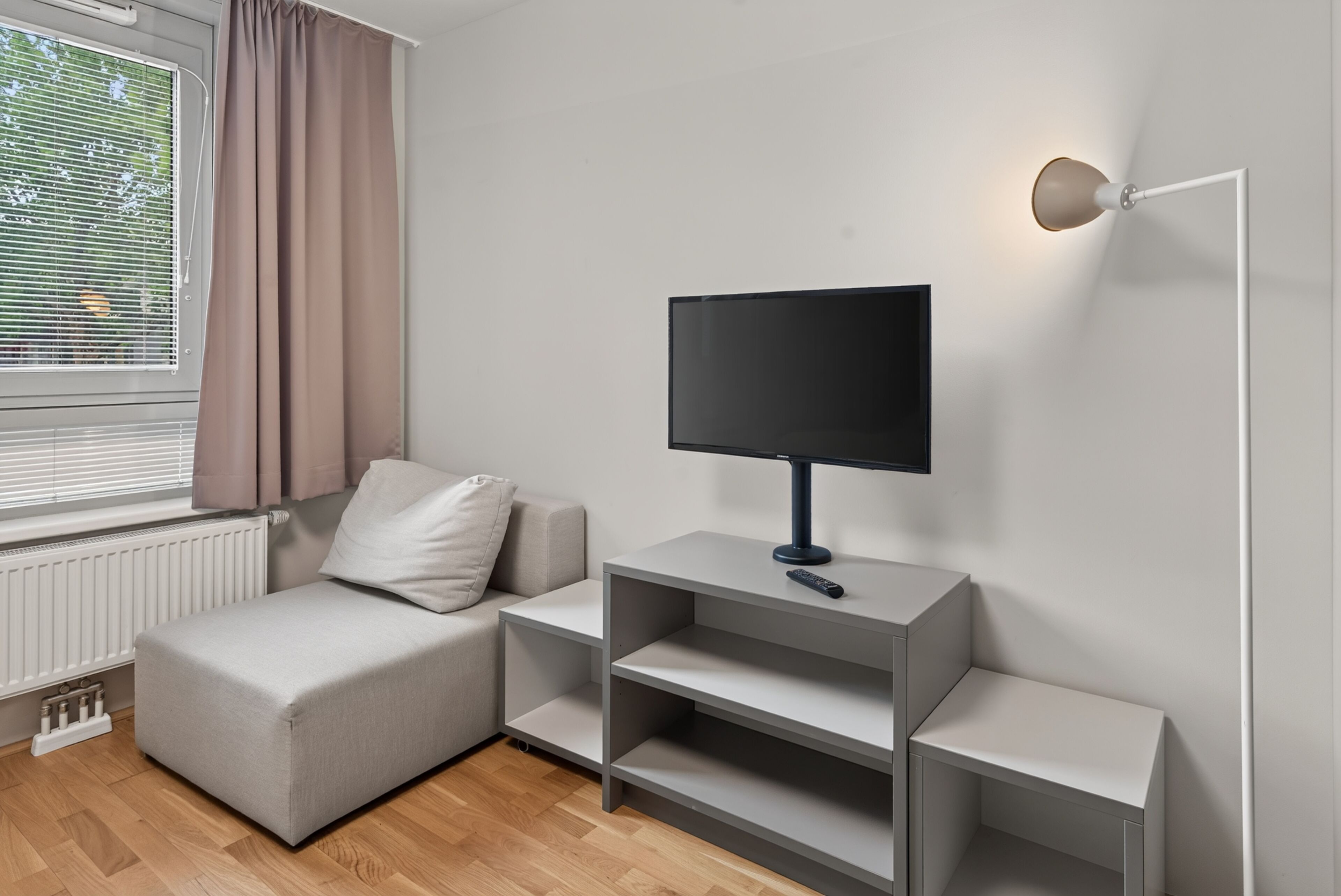 A modern living room with a sofa, a flat-screen TV on a stand, and a wall-mounted light fixture.