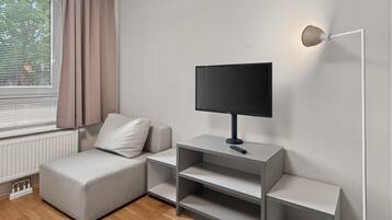 A modern living room with a sofa, a flat-screen TV on a stand, and a wall-mounted light fixture.