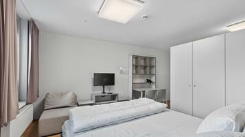 A modern hotel room with a bed, a desk, a chair, a TV, and a wardrobe.