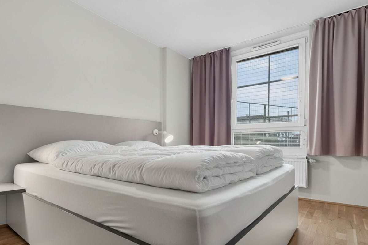Ein modernes Schlafzimmer mit einem Bett, Nachttischlampen, einem Fenster mit Vorhängen und einer Heizung.