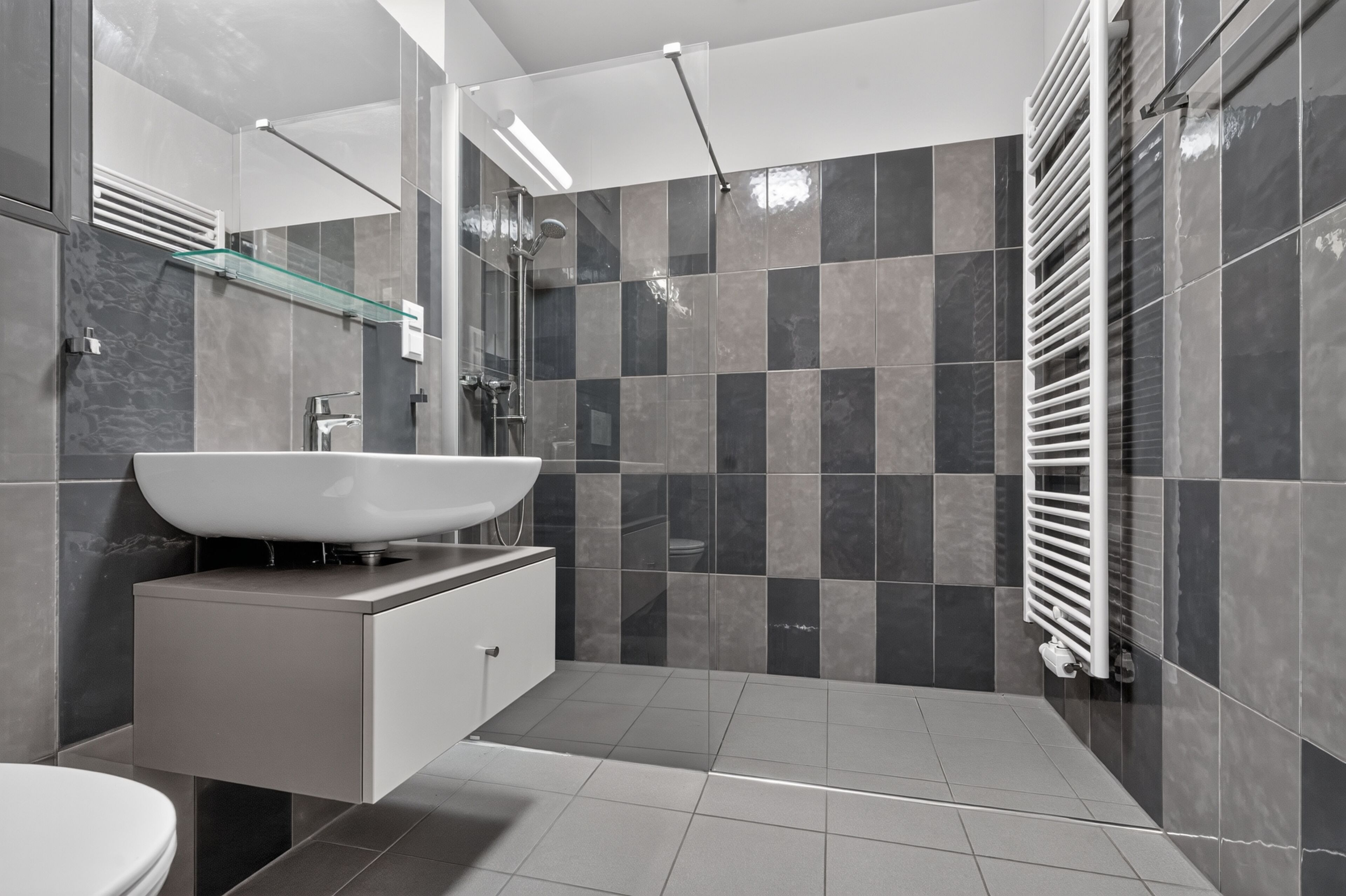 Ein modernes Badezimmer mit einem großen weißen Waschbecken, einer Glasablage und einer begehbaren Dusche.