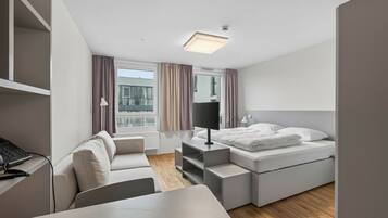 Et moderne hotelværelse med seng, skrivebord, stol og et vindue med gardiner.