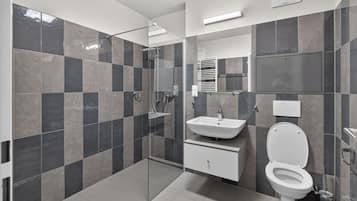Een moderne badkamer met een douchecabine van glas, een witte wastafel en een toilet.